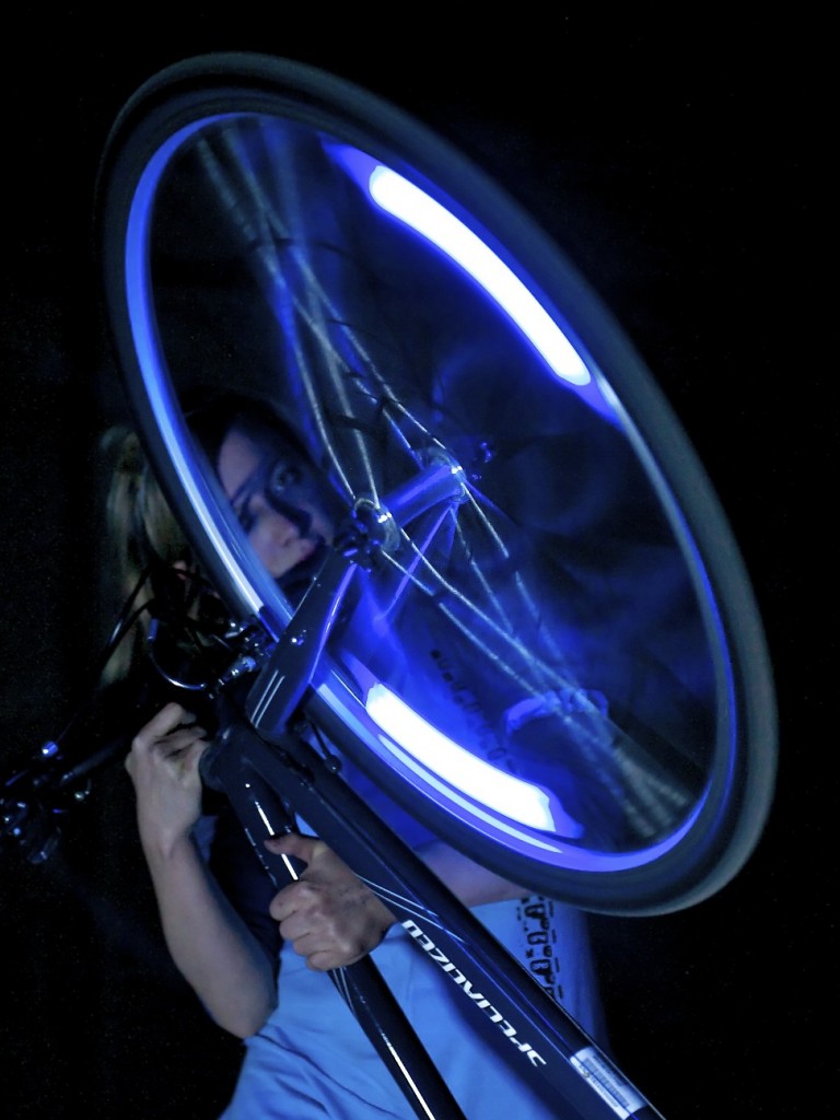 Female performer looking through blue lit, spinning wheel spokes