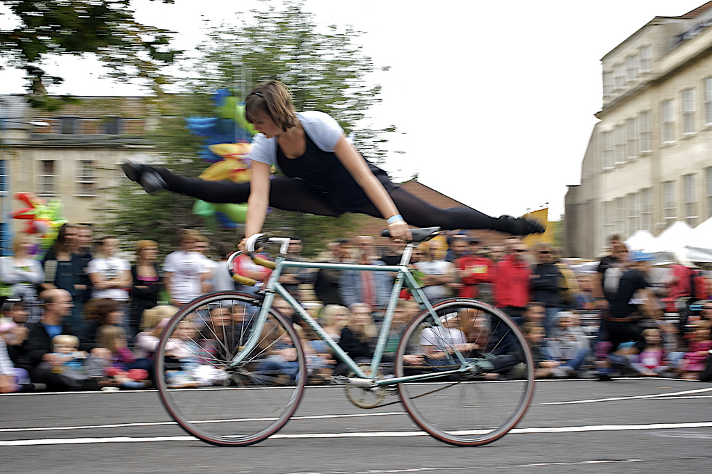 Performer does aerial splits alongside moving bike