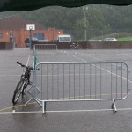 a solitary bike leans against a piece of crowd control barrier at the edge of the empty performance space, during a torrential rainstorm 