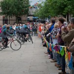 Audience behind bunting as performers on bikes turn into the distance