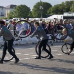 3 performers in a line, pirouette their bikes on the front wheel