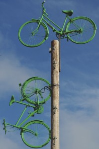 One green painted bicycle sits on top of a disused telegraph pole and another appears 'parked' on the side of the pole
