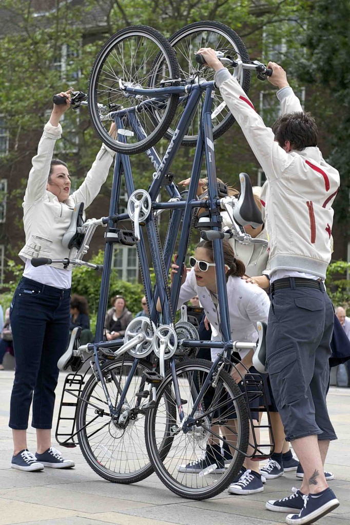 Vanity peers through the frames of two tandems held on their back wheels, representing the lift doors