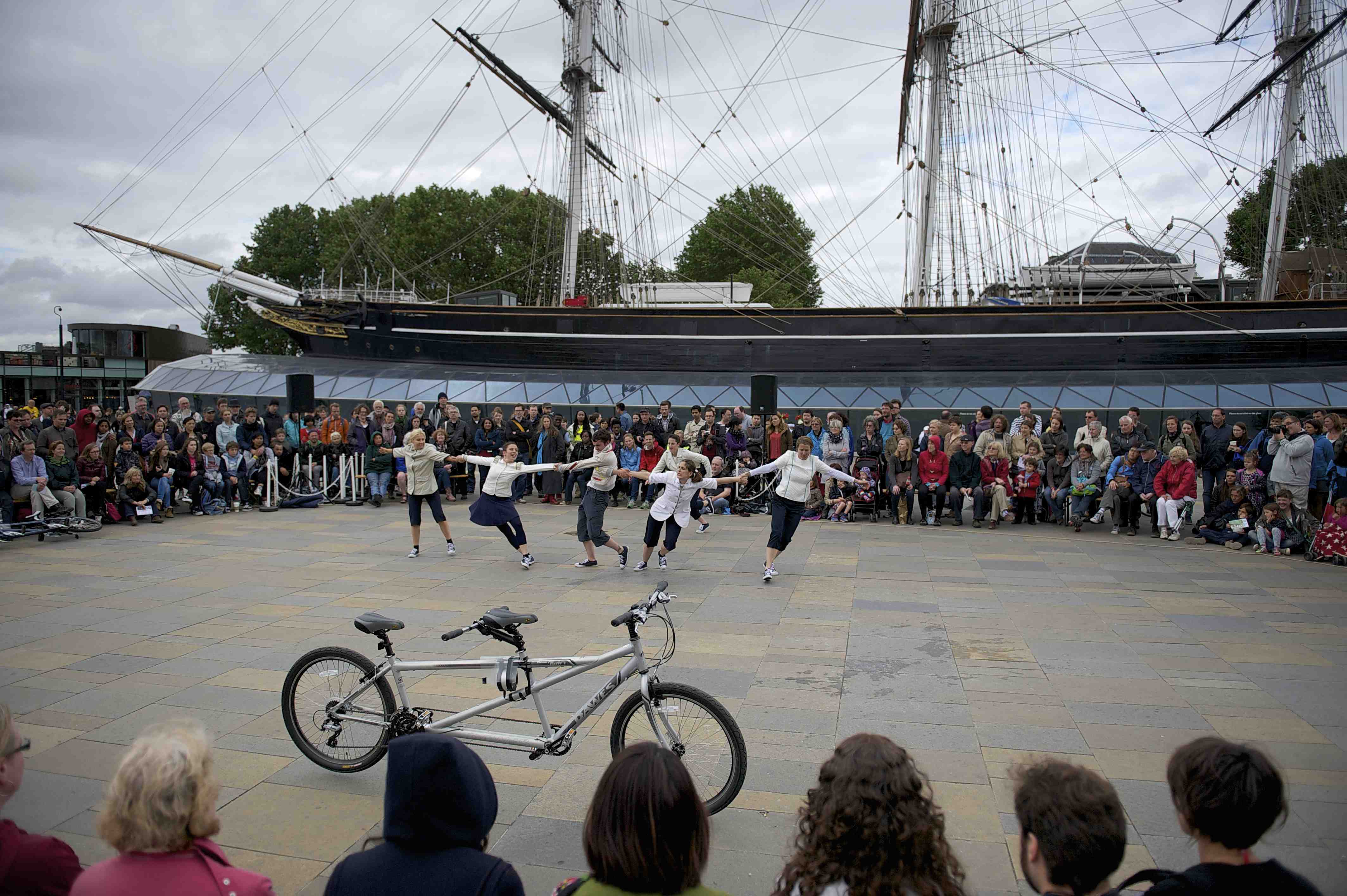 Performers in a line pulling Frustration, surrounded by a large crowd in front of the Cutty Sark